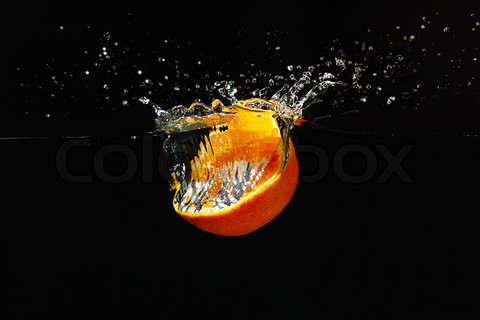 Halved orange falling into the water with a splash on a black background